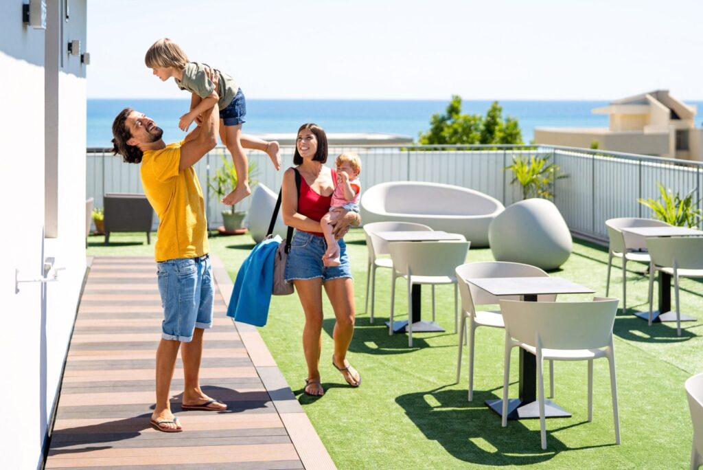 A family enjoys a sunny day on a rooftop terrace with ocean views.