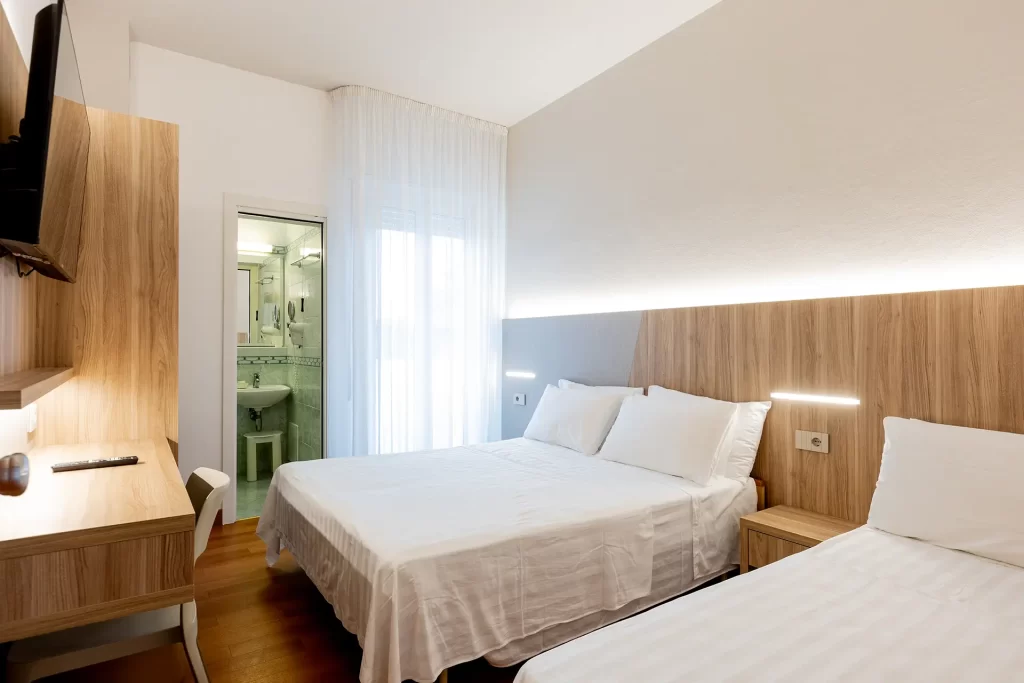 A modern hotel room with twin beds, a desk, and an en-suite bathroom.