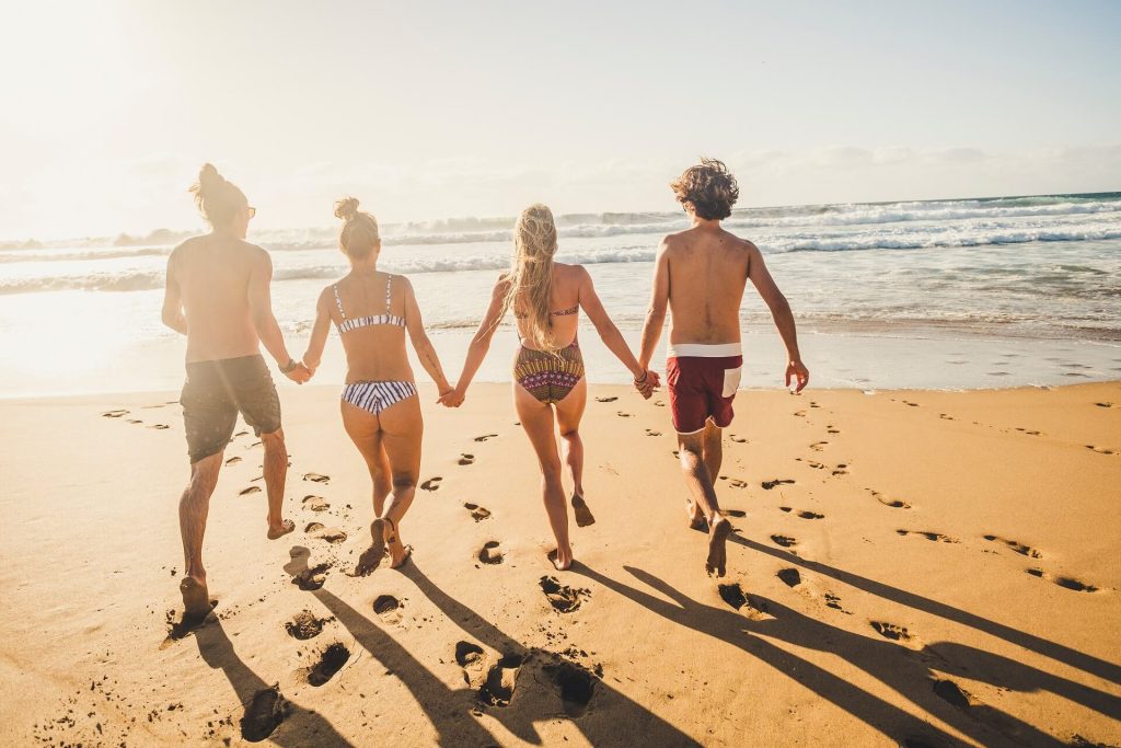 Quattro persone camminano mano nella mano su una spiaggia verso il mare.