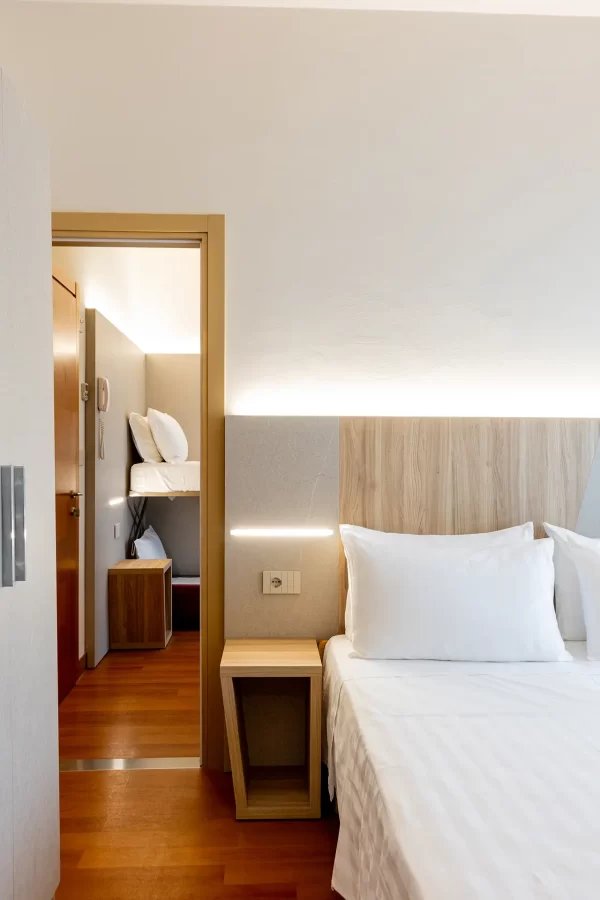 A modern hotel room with a double bed and a view into another room with a bunk bed.