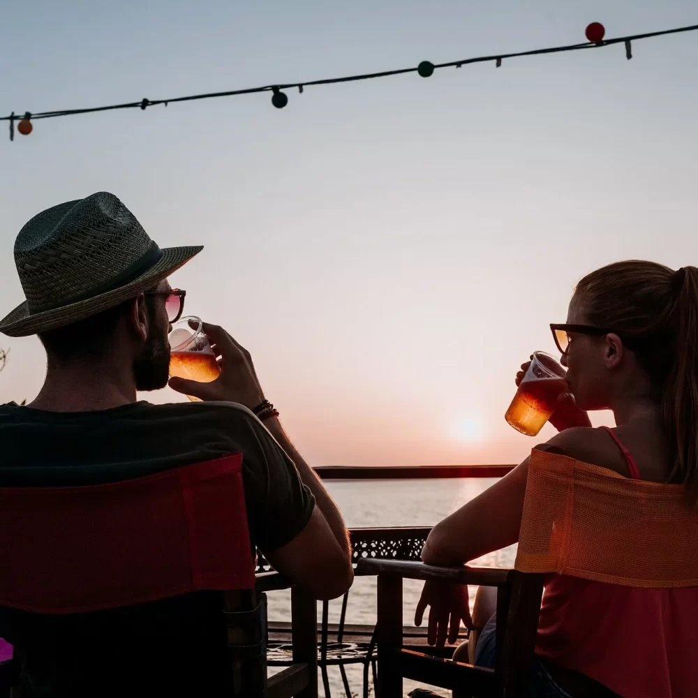 Zwei Personen sitzen bei Sonnenuntergang mit Getränken auf einer Terrasse.